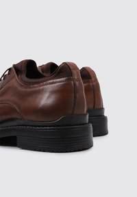 Zapatos de piel marrón con un acabado suave, que presentan un diseño de corte bajo y una suela de goma negra. Detalle de costura notable en las costuras.