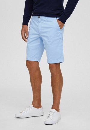 Shorts bleu clair en matière mélange coton, avec fermeture à bouton, poches latérales et coupe décontractée, associés à des baskets blanches.