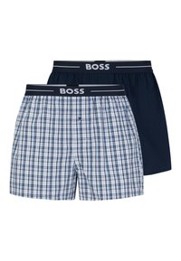 Two pairs of men's boxers: one with a blue and white plaid pattern, the other solid navy. Both have a dark waistband with "BOSS" logo.