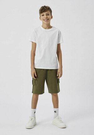 T-shirt bianco a maniche corte, pantaloni cargo olive con tasche laterali, sneaker bianche e calzini bianchi a mezzo polpaccio con logo nero. Stile semplice e casual.