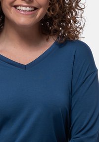 Sininen V-pääntie paita, joka on valmistettu pehmeästä kankaasta, jolla on sileä rakenne. Ominaisuudet löysät hihat ja yksinkertainen, selkeä muotoilu.