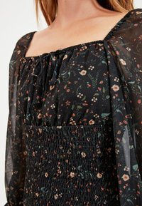 Black floral dress with lightweight sheer sleeves, square neckline, and gathered texture at the waist. Features small colorful flower patterns.