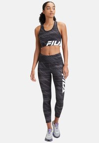 Cropped top sportivo nero e leggings con un motivo testurizzato. Logo Fila in evidenza in bianco. Completato da sneakers grigie con dettagli viola.