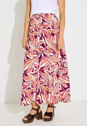 Mujer con falda midi con botones delanteros con estampado de hojas en rosa y naranja, top blanco, pulsera plateada y sandalias de plataforma marrones.