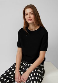 Czarny dzianinowy sweter z krótkim rękawem w połączeniu z plisowaną spódnicą w czarno-białe kropki. Gładka faktura, luźny krój i okrągły dekolt.
