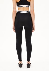 Zwarte legging met een slim fit ontwerp en een hoge tailleband met een wit "ARMEDANGELS" logo. Gladde textuur, rekbare stof, enkel lengte.