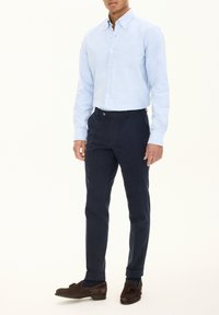 Lichtblauw blouse met knopen, marineblauwe broek, bruine suède instappers. Slim fit, lange mouwen, manchetten met één knoop, eenvoudig kraagontwerp.