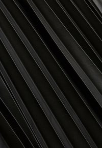 Gros plan sur un tissu en cuir noir plissé avec des plis cousus en diagonale créant un motif texturé.