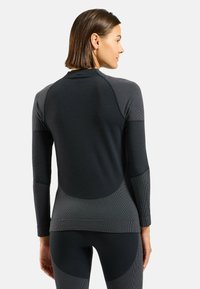 Haut de sport à manches longues en noir et gris, avec un tissu texturé, une coupe ajustée, des panneaux contrastés et un ourlet arrondi.