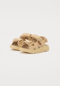 Beige Sandalen mit geflochtenen Stoffriemen, Klettverschlüssen und strukturierten Sohlen sowie einem gepolsterten Fußbett für zusätzlichen Komfort.