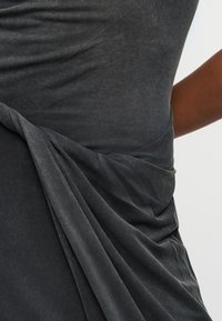 Κοντινό πλάνο του κορμού ενός ατόμου που φοράει φόρεμα από απαλό ύφασμα σκούρου γκρι χρώματος με συγκεντρωμένες πιέτες στη μία πλευρά.