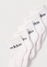 Meias brancas de algodão com punhos canelados, apresentando a marca "adidas" em preto. Dispostas em fila, mostrando sua textura macia e design.