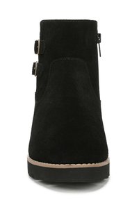 Stivaletto in suede nero con punta arrotondata, zip laterale e due fibbie decorative. La suola presenta un motivo testurizzato per garantire aderenza.