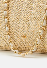 Gros plan d'un sac tissé beige avec un motif texturé et une sangle chaîne dorée entrelacée de cuir beige.