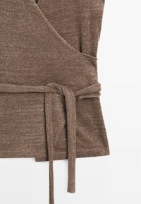 Haut cache-cœur marron en tissu doux et texturé avec une ceinture nouée à la taille. Présente un profond décolleté en V et une silhouette fluide.