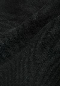 Gros plan d'un tissu noir avec une texture douce et tissée, ainsi que des plis subtils créant des lignes diagonales à la surface.