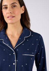 Haut de pyjama bleu marine avec motif étoilé blanc ; avec poche, col pipé et boutons ; en tissu doux.