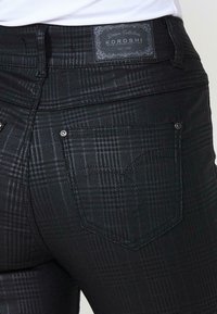 Fekete farmernadrág finom kockás mintával, derékrészen címkével, és két hátsó zsebével fém részletekkel.