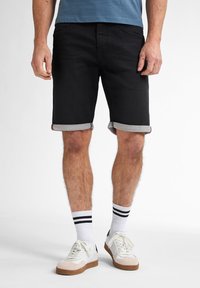 Schwarze Denim-Shorts mit umgeschlagenen Säumen, mit fünf Taschen ausgestattet. Tragen Sie sie mit weißen Sneakers und gestreiften Socken für einen lässigen Look.