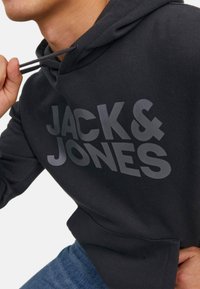 Black hoodie with gray "JACK & JONES" logo, drawstring hood, and front pocket. Cotton blend fabric, relaxed fit with a soft texture.