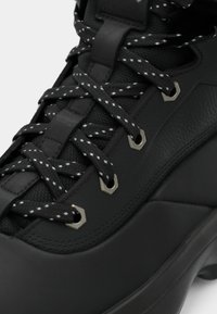 Czarne buty trekkingowe z teksturowanej skóry i siateczkowego materiału, z metalowymi oczkami i kontrastującymi szarymi sznurówkami. Wzmocniony obszar palców.