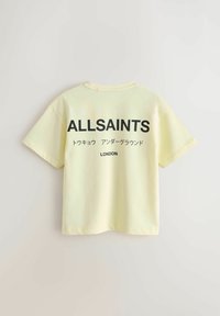 Svetložlté tričko s krátkym rukávom s nápisom "ALLSAINTS," japonským textom a slovom "LONDON" vytlačeným čiernou farbou na zadnej strane.