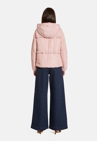 Vadderad, ljusrosa jacka med huva, volangdetaljer längs sömmarna och elastisk midja, tillsammans med vida mörka denimbyxor.