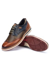 Herresko i nuancer af brun og mørkegrøn læder, med brogue-detaljer, runde tåer og gummisåler med mønstrede skridser.