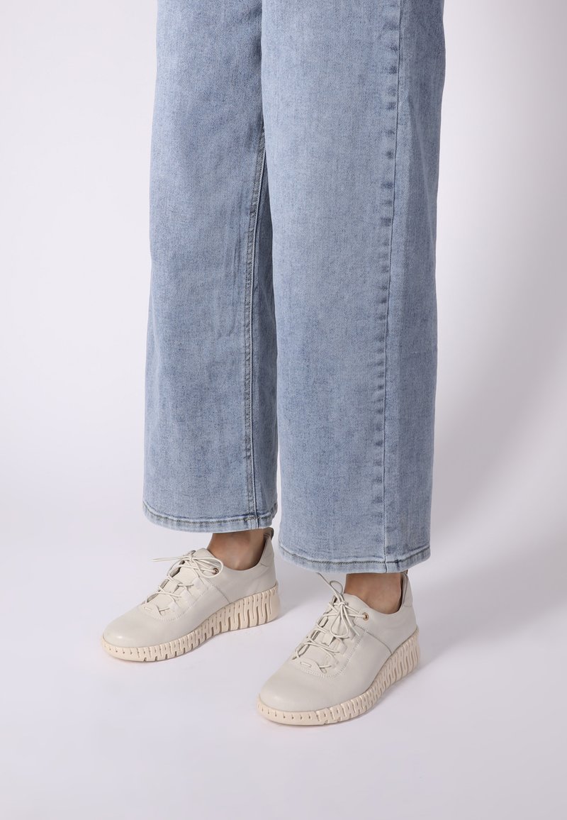 Helle beige Sneakers mit Schnürdesign, strukturierten Gummisohlen und einer klobigen, gerillten Plattform. Kombiniert mit hellblauen weit geschnittenen Jeans.