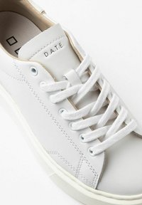 Sneaker bianco in pelle liscia, con lacci rotondi, dettagli di cucitura e logo sulla linguetta. Design minimalista, suola in gomma.