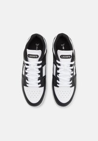 Zapatillas negras y blancas con un empeine de cuero liso, punta perforada, cordones blancos y el logotipo de Lacoste en la lengüeta y en el lateral.