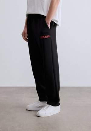 Czarne spodnie dresowe z bocznymi kieszeniami, z czerwonym logo "Calvin Klein". Wykonane z miękkiego materiału, mają luźny krój i elastyczną talię.