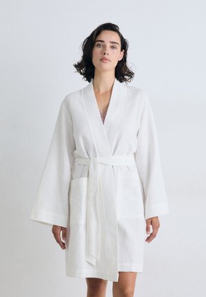 Robe bianca con un motivo testurizzato, maniche lunghe, vita con cintura e tasche frontali. Tessuto leggero adatto per l'abbigliamento da casa.