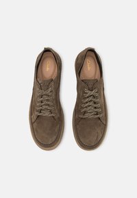 Chaussures en daim marron à texture lisse, bout arrondi et lacets ton sur ton contrastants. Elles présentent un détail surpiqué tout autour du bord et une semelle claire.