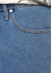 Světlé modré džínové kalhoty s předním kapsou, viditelným kontrastním prošitím a standardním pasem s kovovým knoflíkem.