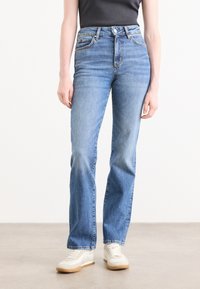 Lys blå denim jeans med høy midje, rett ben design, fem-lomme stil, og hvite og brune sneakers. Jeansen har en glatt tekstur og minimal detaljering.