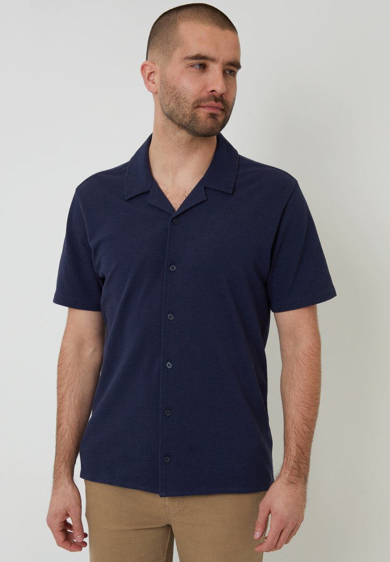 Korte mouwen, button-up shirt van donkerblauwe stof met een gladde textuur, voorzien van een verspreide kraag en zwarte knopen. Minimalistisch ontwerp.
