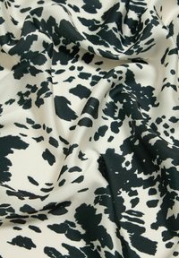 Tissu à motif noir et blanc avec une texture lisse, présentant des taches irrégulières sur un fond crème clair.