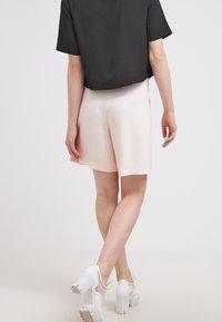 Lichtroze shorts met een gladde textuur, met een losse pasvorm en omgezoomde randen, gecombineerd met een zwart crop-top en witte hakken.