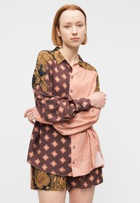 Μπλούζα με μακριά μανίκια που διαθέτει ανάμεικτα σχέδια σε καφέ και ροζ, με γιακά και κουμπιά στο εμπρόσθιο μέρος με χρυσές λεπτομέρειες. Συνδυάζεται με σορτς με σχέδια.