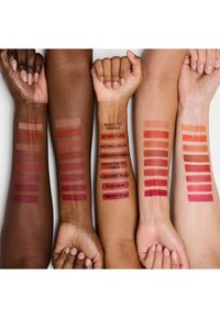 Échantillons de rouge à lèvres sur des bras de différentes teintes de peau ; les nuances comprennent des rouges profonds, des roses doux et des tons nude chauds, étiquetés avec le nom de chaque couleur.