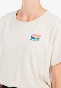Bawełniana koszulka w jasnym kremowym kolorze, z okrągłym dekoltem i krótkimi rękawami, z haftowanym zachodem słońca i napisem "PROTEST" w niebieskim i różowym kolorze.
