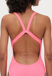 Costume da bagno intero rosa con schiena bassa, spalline incrociate e materiale morbido ed elasticizzato con dettagli di cucitura sottili.