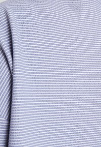 Ljusblått tyg med ett texturerat mönster och växlande tunna vita ränder som skapar en subtil visuell kontrast.