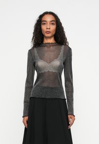 Must have musterlane varrukatega must topp, millel on läbipaistev ja sädelev tekstuur, sakiline kaelus ja lõpp, mille alla on kihtidest saadud pitsist rinnahoidja, kantud koos musta seelikuga.