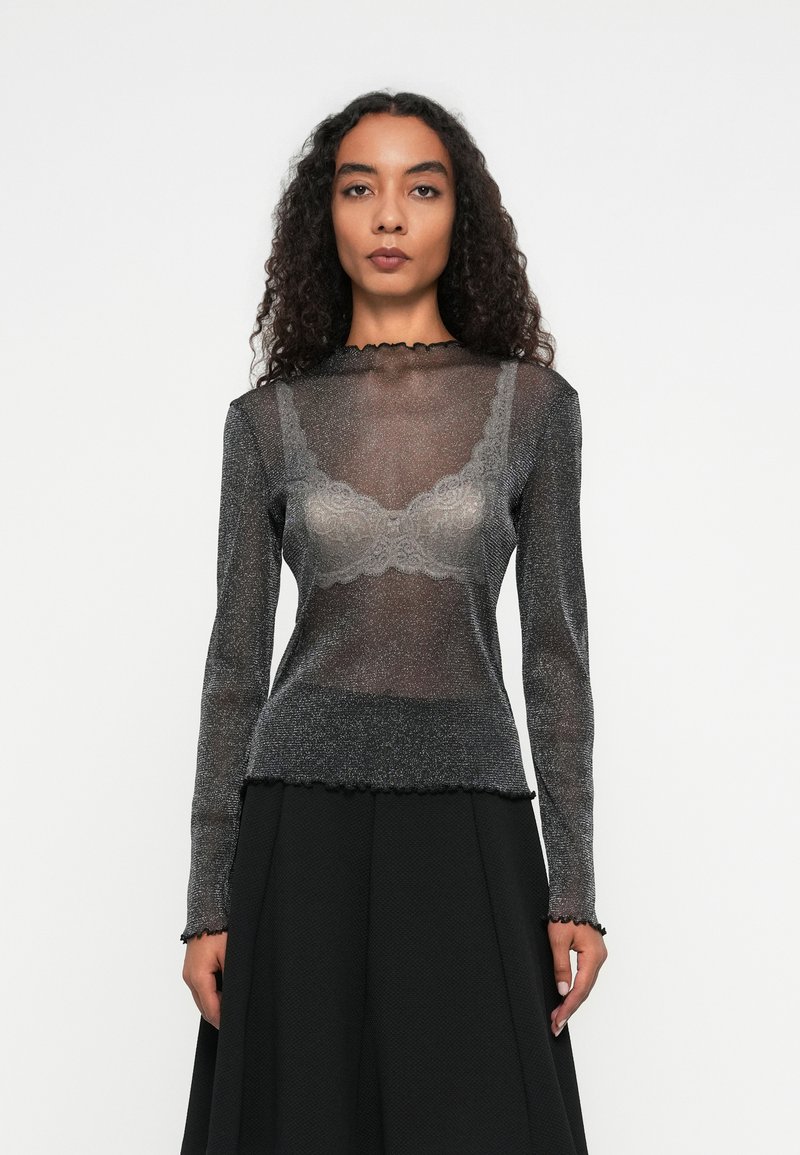 Must have musterlane varrukatega must topp, millel on läbipaistev ja sädelev tekstuur, sakiline kaelus ja lõpp, mille alla on kihtidest saadud pitsist rinnahoidja, kantud koos musta seelikuga.