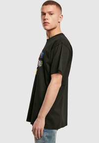 Sort bomulds T-shirt med korte ærmer og en afslappet pasform. Har farverig grafisk tekst på fronten. Båret med lyseblå jeans.