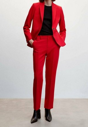 Conjunto de blazer y pantalones ajustados rojos, confeccionado en una tela suave. Presenta un corte Slim Fit, solapas de muesca y bolsillos. Combinado con tacones negros.