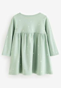 Ljusgrön långärmad klänning för små barn med små vita trädmönster och en volangdetalj under bröstet.