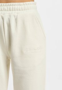 Lyscreme sweatpants lavet af blødt bomuldsjersey, med en afslappet pasform, elastisk talje og diskret broderet tekst på låret.